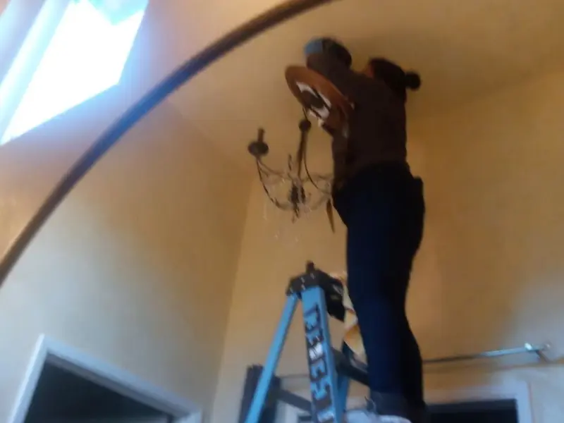 Electrician installing a chandelier in a Foster residence